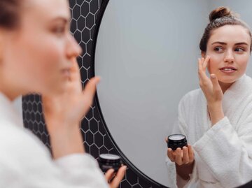 Frau schaut in den Spiegel und cremt sich ein | © Getty Images/Halfpoint Images