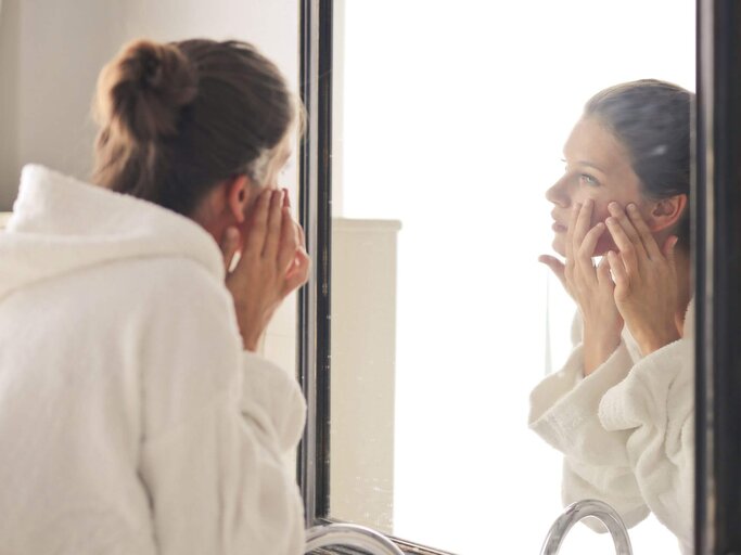 Frau drückt an Gesichtshaut herum im Spiegel | © Getty Images/Wirestock