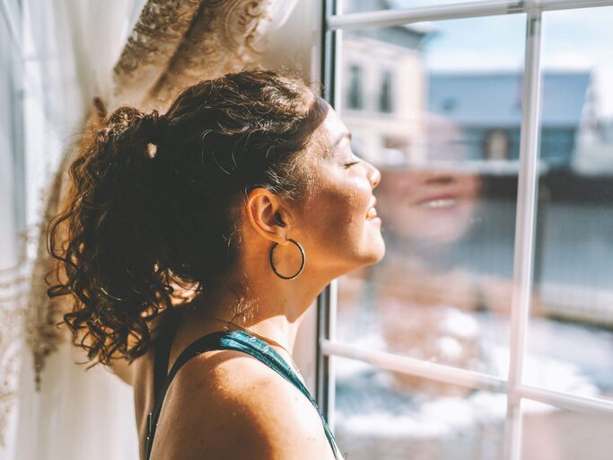 Person steht am Fenster in Sonne | © Getty Images/Olga Rolenko