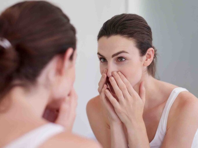 Junge Frau checkt ihre Gesichtshaut im Spiegel | © Getty Images/jeffbergen