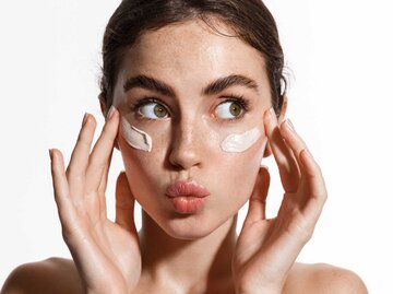 Junge Frau trägt Skincare Produkte auf ihre Haut auf und macht einen Kussmund | © Adobe Stock/Liubov Levytska
