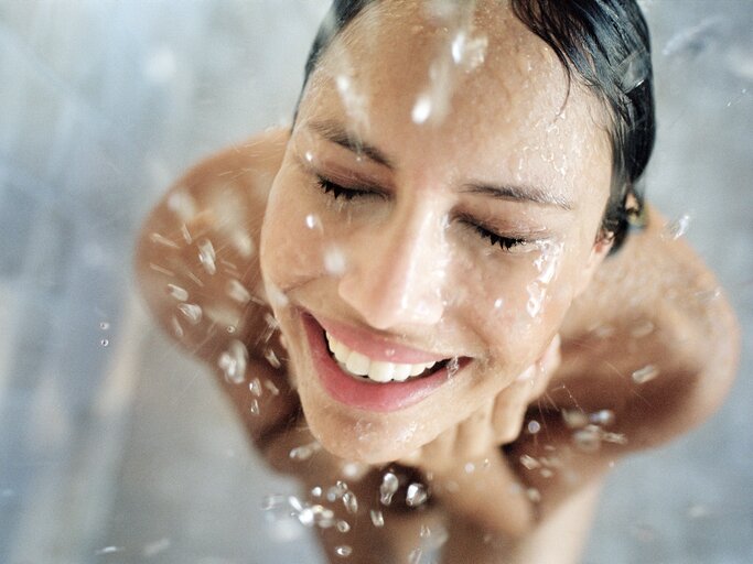 Frau steht lächelnd unter der Dusche | © Getty Images/Laurence Monneret