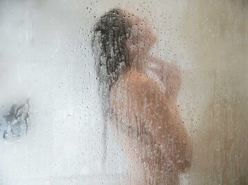 Frau hinter der Glasscheibe einer Dusche. | © Getty Images / Zero Creatives