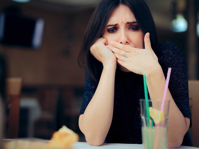 Frau sitzt im Restaurant am Tisch und hat Schluckauf. | © Getty Images / nicoletaionescu