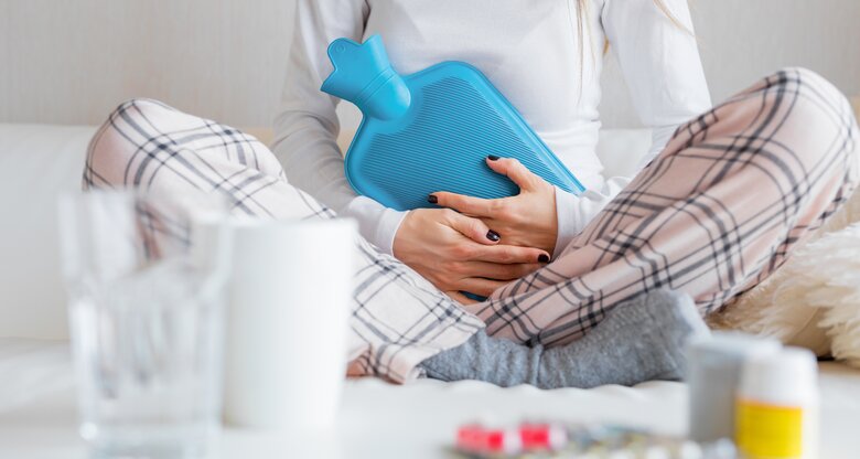 Frau sitzt auf ihrem Bett mit einer Wärmflasche | © Getty Images/grinvalds