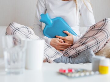 Frau sitzt auf ihrem Bett mit einer Wärmflasche | © Getty Images/grinvalds