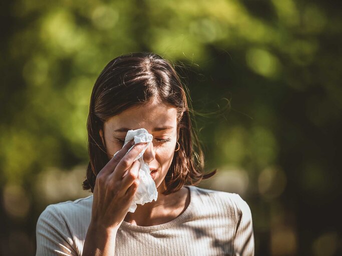 Frau hat Heuschnupfen und hält sich in der Natur ein Taschentuch vor die Augen. | © Getty Images / RealPeopleGroup
