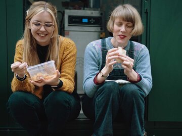Zwei Frauen sitzen draußen und essen  | © Getty Images/Sarah Mason
