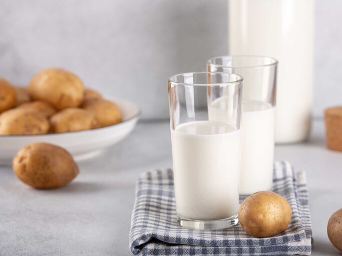 Zwei Gläser Milch stehen neben Kartoffeln auf dem Tisch. | © Getty Images / Elizaveta Elesina
