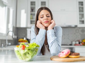 Junge Frau wählt zwischen Donuts und Gemüsesalat | © Getty Images/bulatovic