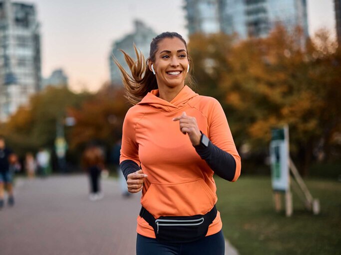 Frau lächelt während sie joggt und Musik hört | © Getty Images/Drazen Zigic