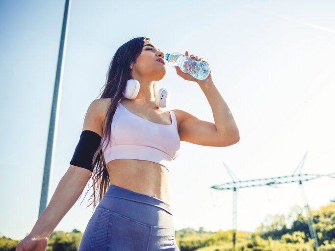 Eine junge Frau hebt eine Wasserflasche an ihren Mund | © GettyImages/Jelena Stanojkovic