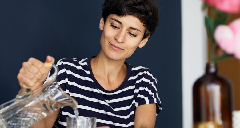 Eine junge Frau schenkt sich Wasser ein | © GettyImages/Westend61