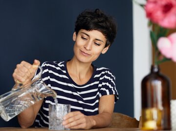 Eine junge Frau schenkt sich Wasser ein | © GettyImages/Westend61