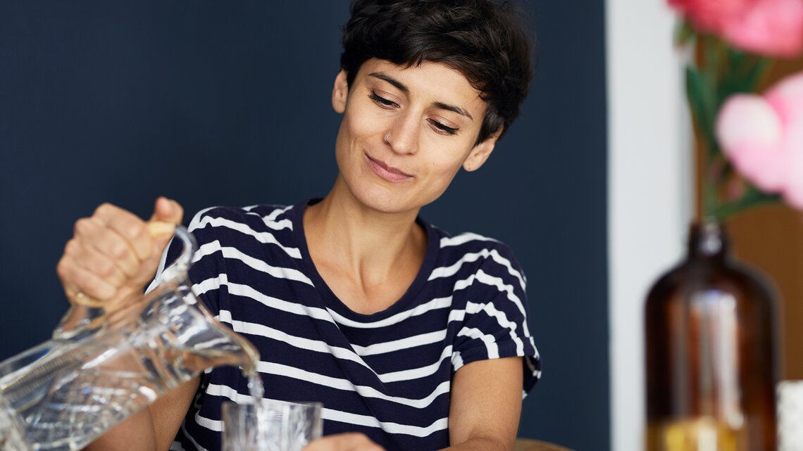 Eine junge Frau schenkt sich Wasser ein | © GettyImages/Westend61
