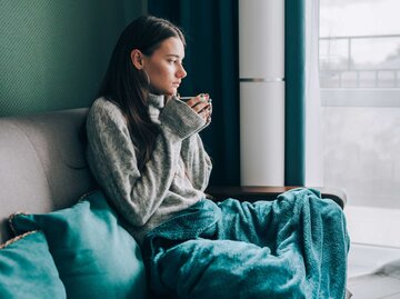 Frau sitzt mit einer Decke und Tasse in der Hand auf der Couch | © Getty Images/Olga Rolenko