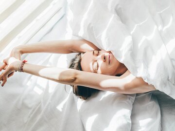 Eine Frau streckt sich genüsslich im Bett | © GettyImages/Maria Korneeva