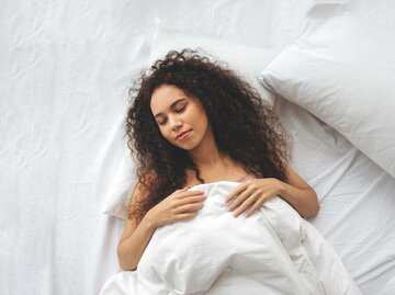 Junge Frau schläft zufrieden in weißer Bettwäsche | © Getty Images/Maryna Terletska