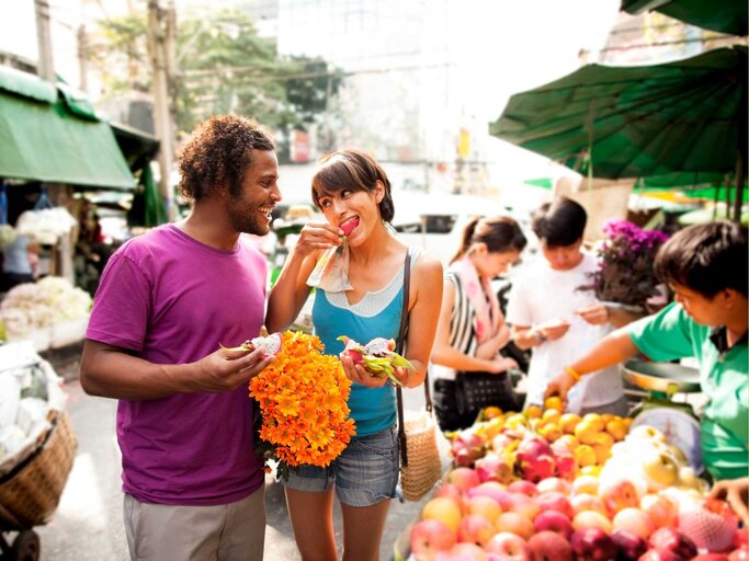 Frau läuft mit Mann über einen Markt und isst etwas | © Getty Images/Jim Purdum