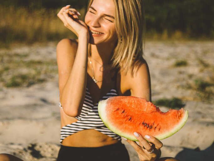 Junge Frau sitzt auf dem Boden und isst eine Wassermelone. | © Getty Images / Iuliia Bondar