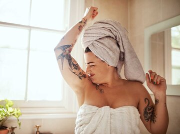 Frau steht mit Handtuch im Bad und riecht unter ihren Armen. | © Getty Images / PeopleImages