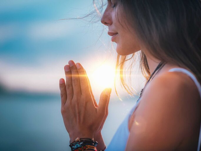 Junge Frau meditiert mit geschlossenen Augen und praktiziert Yoga mit den Händen in Gebetsposition. | © Getty Images/microgen