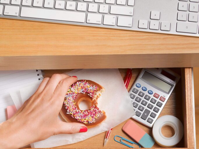 Hand greift nach Donut in Schreibtischschublade | © Getty Images/Peter Dazeley