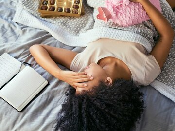 Frau liegt mit Periodenschmerzen im Bett | © Getty Images/LaylaBird