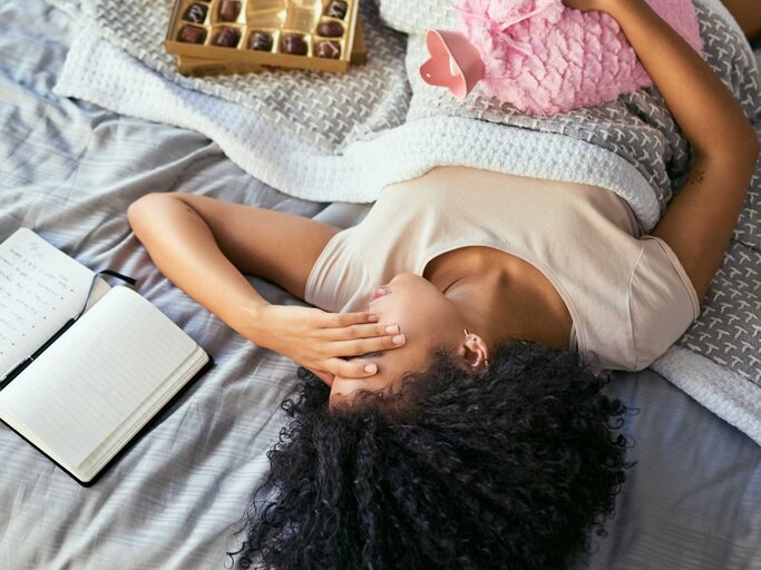 Frau liegt mit Periodenschmerzen im Bett | © Getty Images/LaylaBird