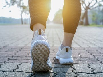 Frauenfüße in Turnschuhen treten auf dem Asphalt auf | © GettyImages/boonchai wedmakawand