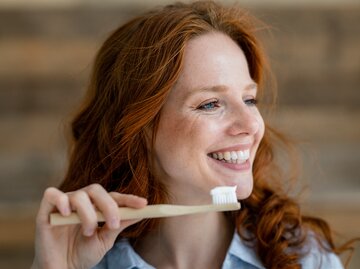 Junge Frau lächelt und hält eine Zahnbürste mit Zahnpasta | © GettyImages/Westend61