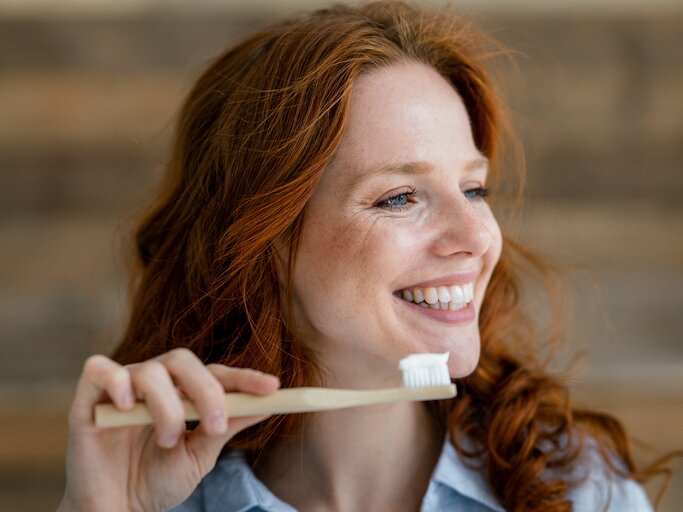 Junge Frau lächelt und hält eine Zahnbürste mit Zahnpasta | © GettyImages/Westend61