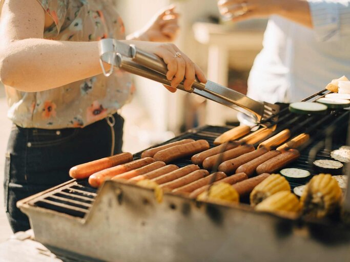 Frau grillt Würstchen und Mais auf einem großen Grill | © Getty Images/Maskot