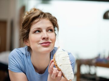 Eine Frau lächelt und isst eine Scheibe Brot mit Aufstrich | © GettyImages/Fabrice LEROUGE