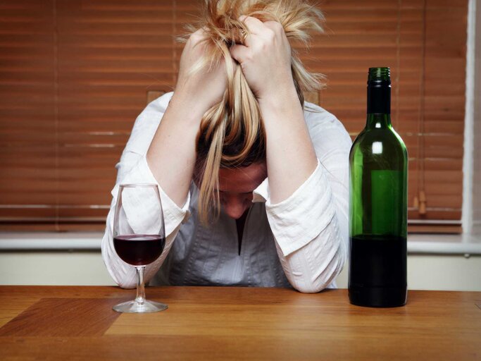 Blonde Frau hat den Kopf auf den Tisch gelegt, vor ihr steht Wein | © Getty Images/Carole Gomez