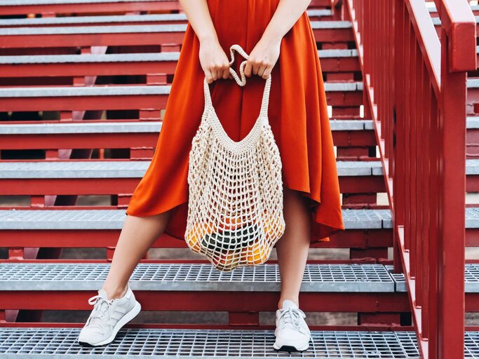 Frau in rotem Kleid trägt eine Einkaufstasche | © Getty Images/Olena Ruban