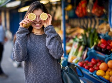 Frau auf einem Markt hält sich Zitronenhälften vor die Augen und lacht. | © Getty Images/ Westend61