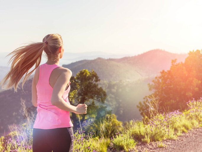 Frau mit blonden Haaren und pinkem Oberteil geht in der Natur joggen | © gettyimages.de / yoh4nn