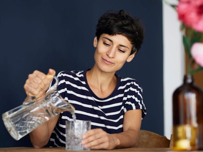 Frau schenkt sich ein Glas Wasser ein | © Getty Images/Westend61