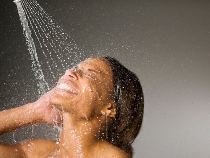 Junge Frau steht unter der Dusche und lacht | © Getty Images/John Lund
