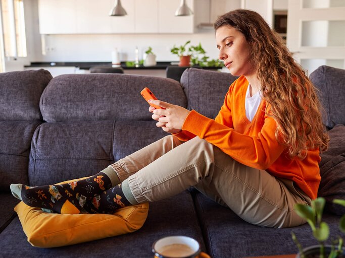 Frau mit orangefarbenem Pulli sieht auf ihr Handy | © Getty Images/Jose Martinez Calderon