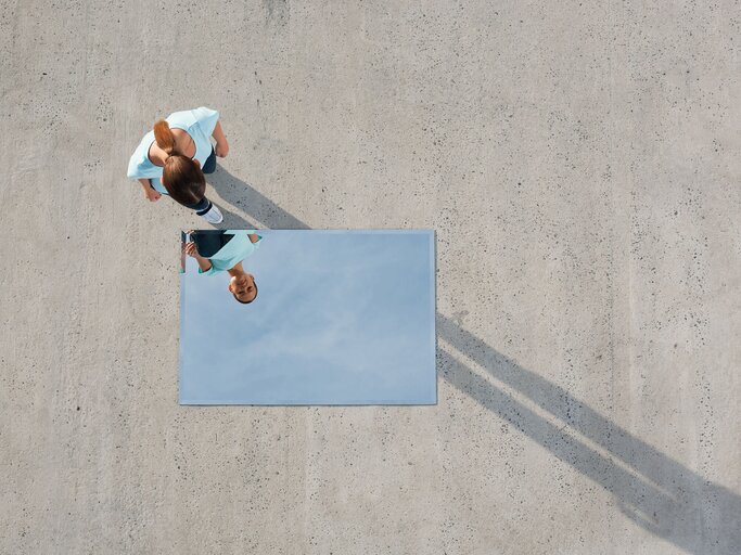 Frau sieht sich im Spiegel an, der auf dem Boden liegt | © Getty Images/Martin Barraud