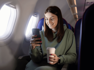 Frau mit Kaffee und Handy im Flugzeug | © Getty Images/RgStudio