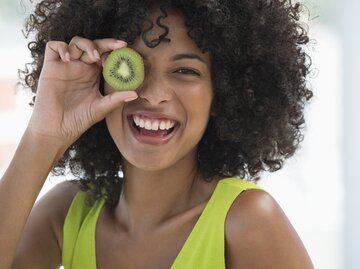 Lachende Frau mit Kiwi in der Hand | © Getty Images/Eric Audras