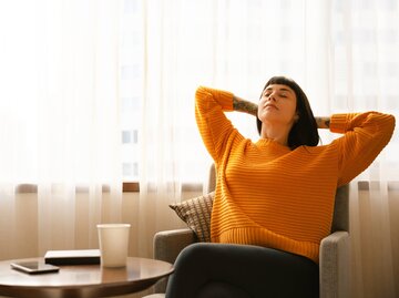 Junge Frau lehnt sich entspannt im Sessel zurück | © Getty Images/Marco_Piunti