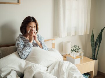 Frau liegt mit einer Erkältung im Bett und schnäuzt ins Taschentuch | © Getty Images/staticnak1983