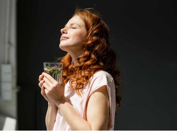 Rothaarige Frau hält Tee in der Hand und genießt die ersten Sonnenstrahlen | © Getty Images/Westend61