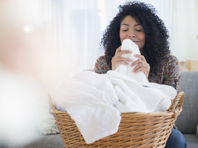 Frau riecht an frisch gewaschener Wäsche aus dem Wäschekorb | © Getty Images/JGI/Jamie Grill