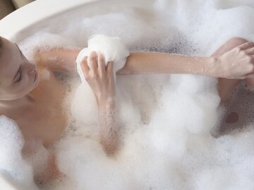 Frau sitzt in schaumiger Badewanne und wäscht sich | © Getty Images/Justin Pumfrey