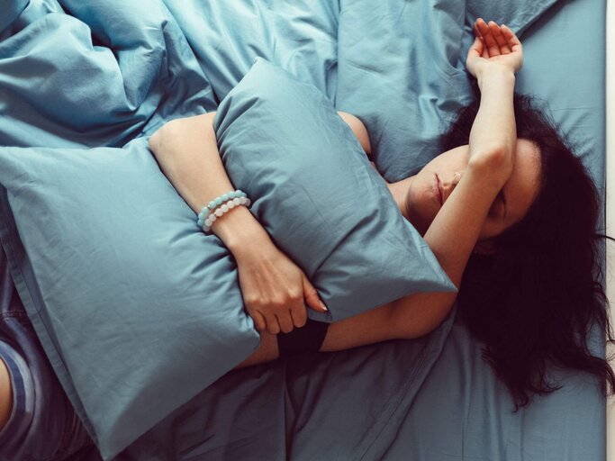Frau liegt verkatert im Bett | © Getty Images/Martin Dimitrov